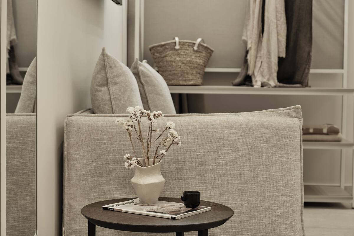 Een moderne woonkamer met een bank, een klein rond tafeltje en een vaas met gedroogde bloemen.