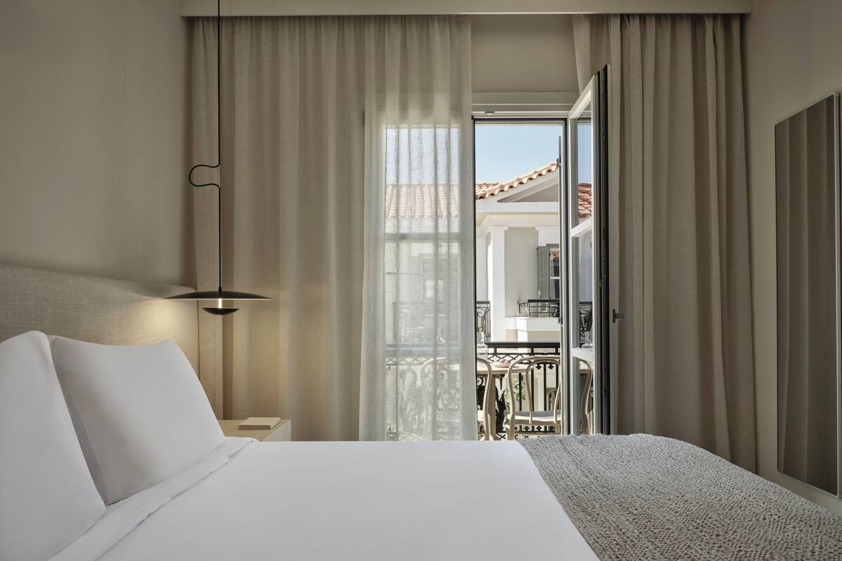 Een hotelkamer met een bed, nachtkastje, lamp en uitzicht op een balkon.
