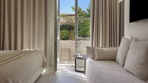 A modern hotel room with a bed, a sofa, a small table, and a TV. - Doryssa Method Hotel (Samos)