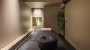 A spa room with a massage table, a black massage chair, and a large potted plant. - Doryssa Method Hotel (Samos)