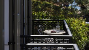 A balcony with a round table, two chairs, a glass bottle, and a glass.
