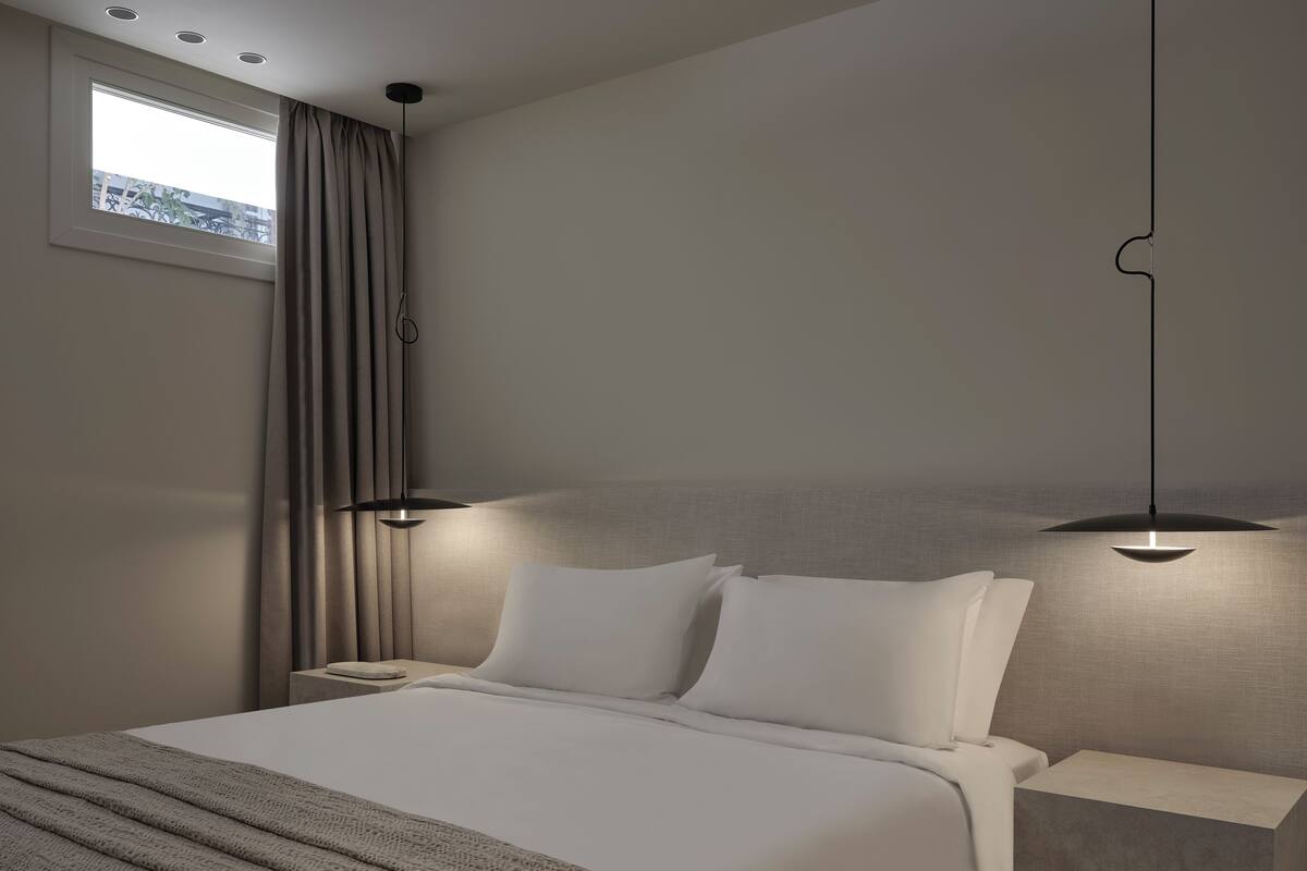 Een moderne hotelkamer met een groot bed, twee nachtkastjes, een raam met gordijnen en een hanglamp.