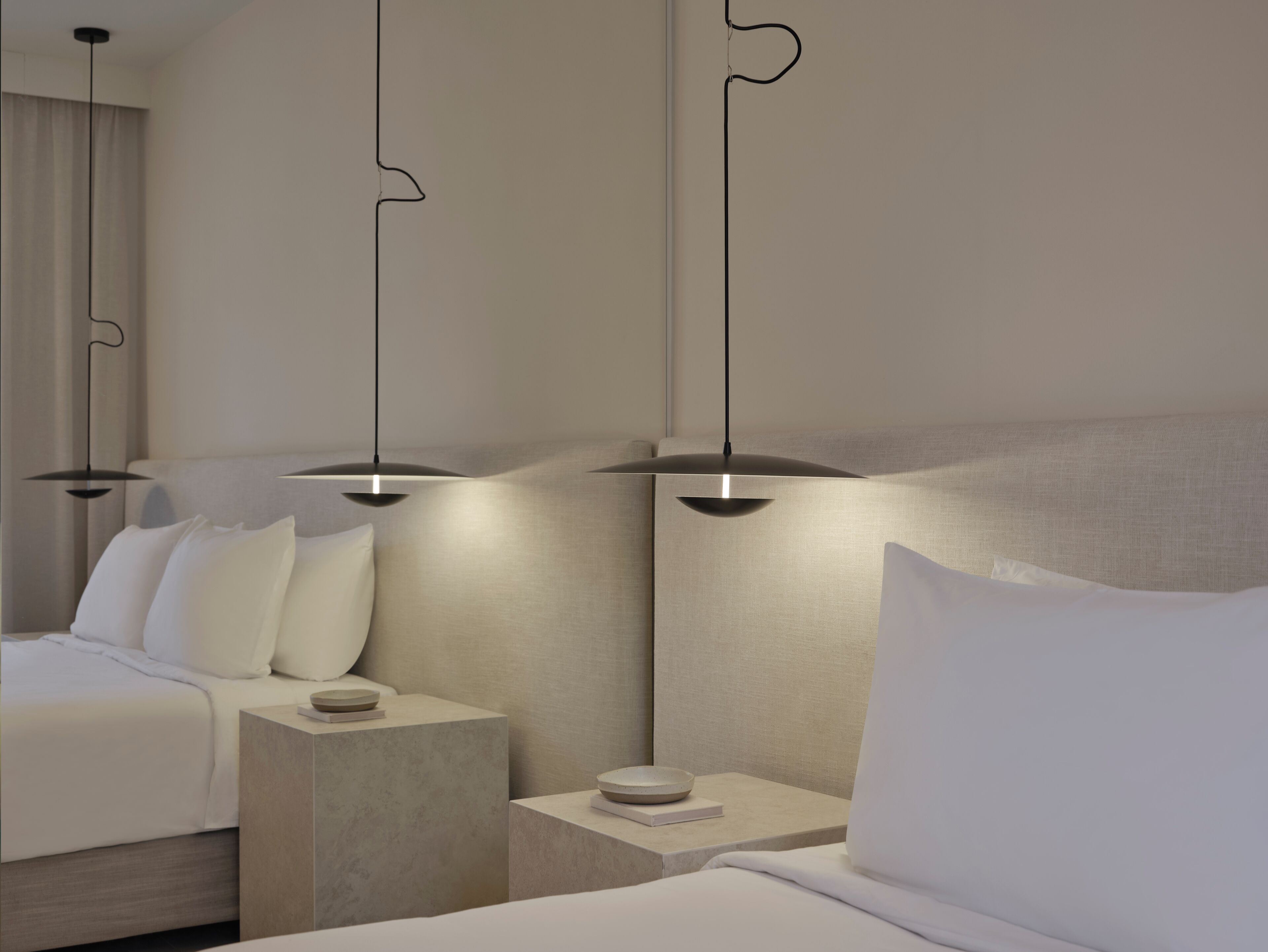 A modern hotel room with a large bed, two bedside tables, and pendant lights.