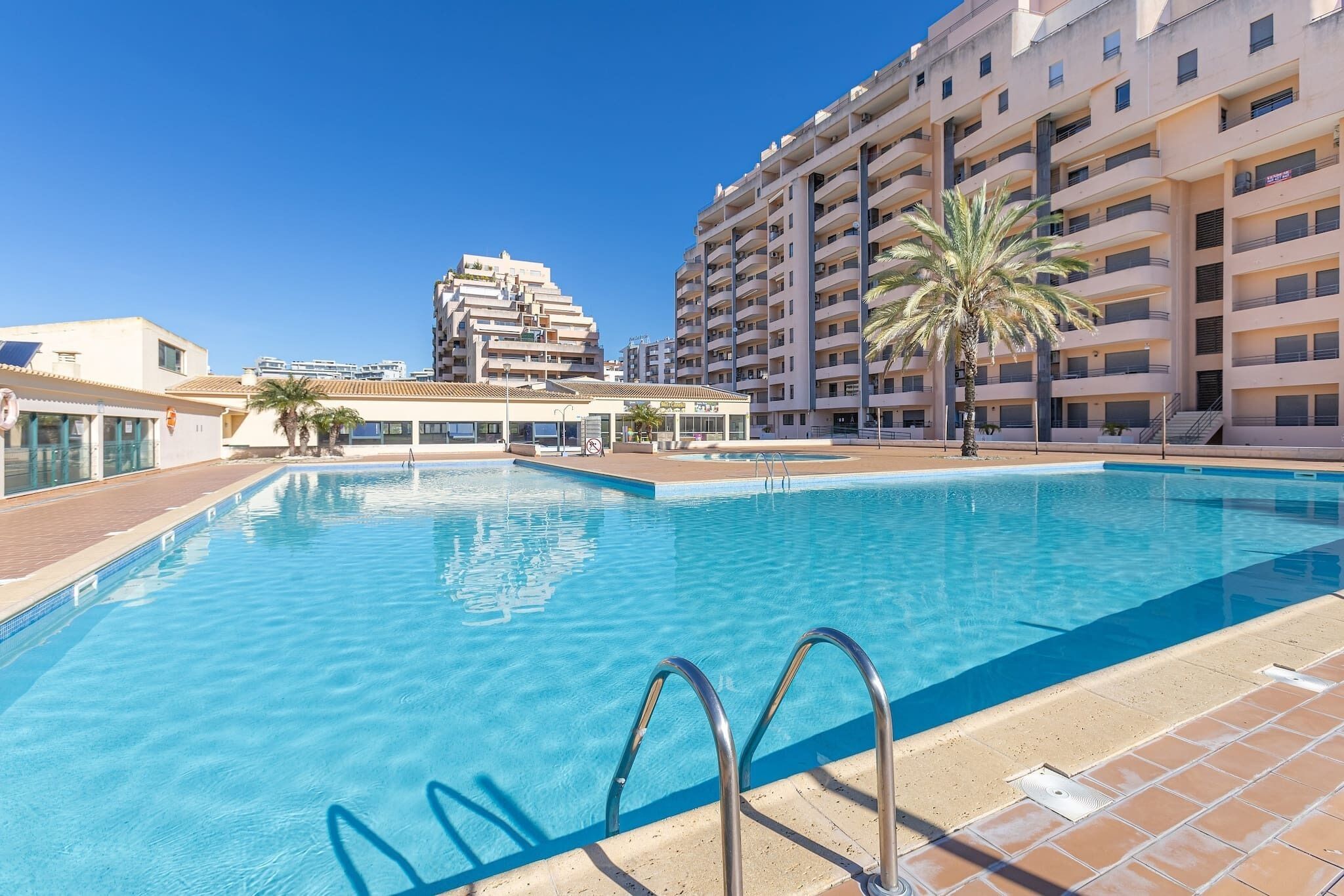 A swimming pool with a clear blue water, surrounded by a tiled deck.