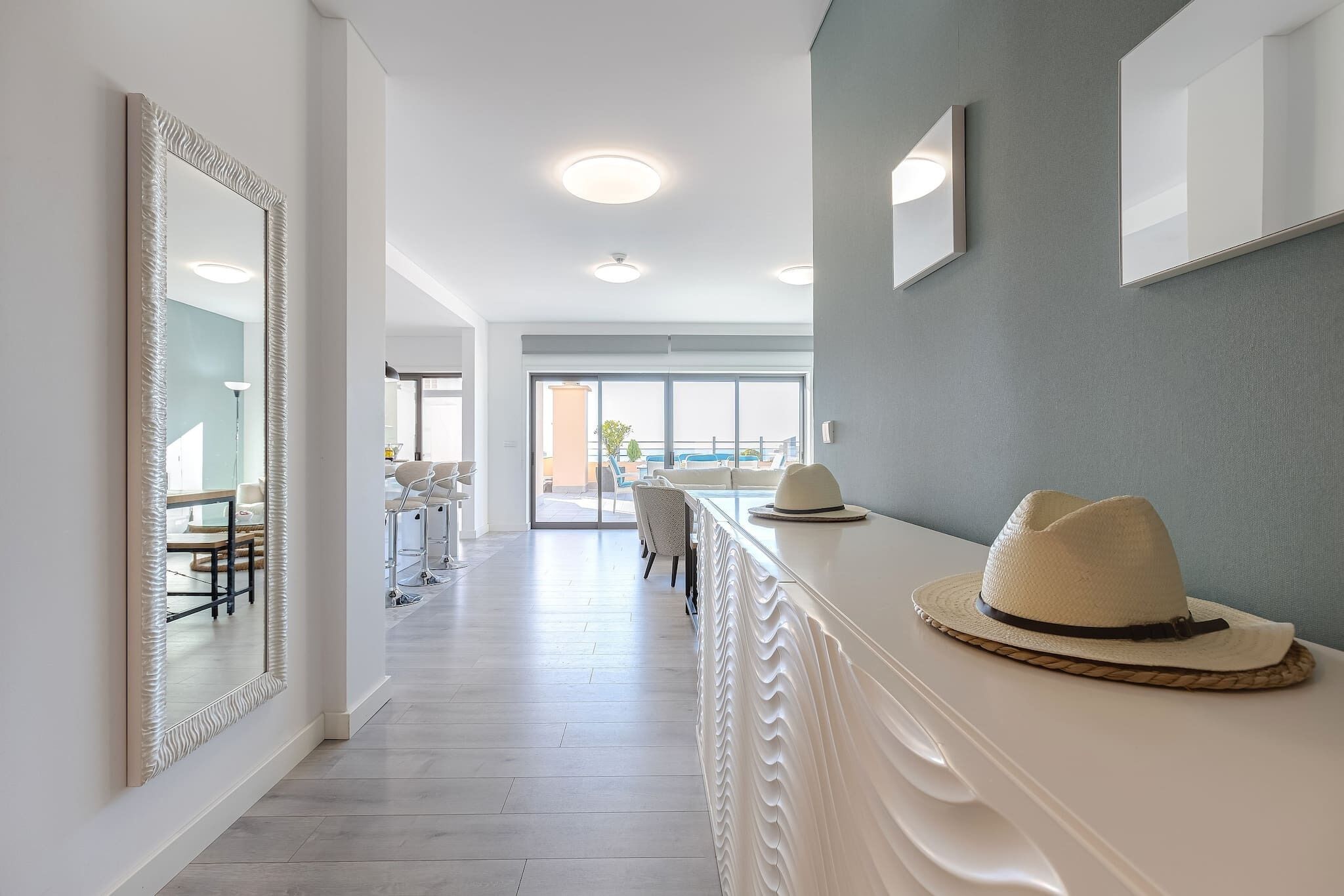 A modern hotel lobby with a long reception desk, a large mirror, and a view of the dining area and outside.