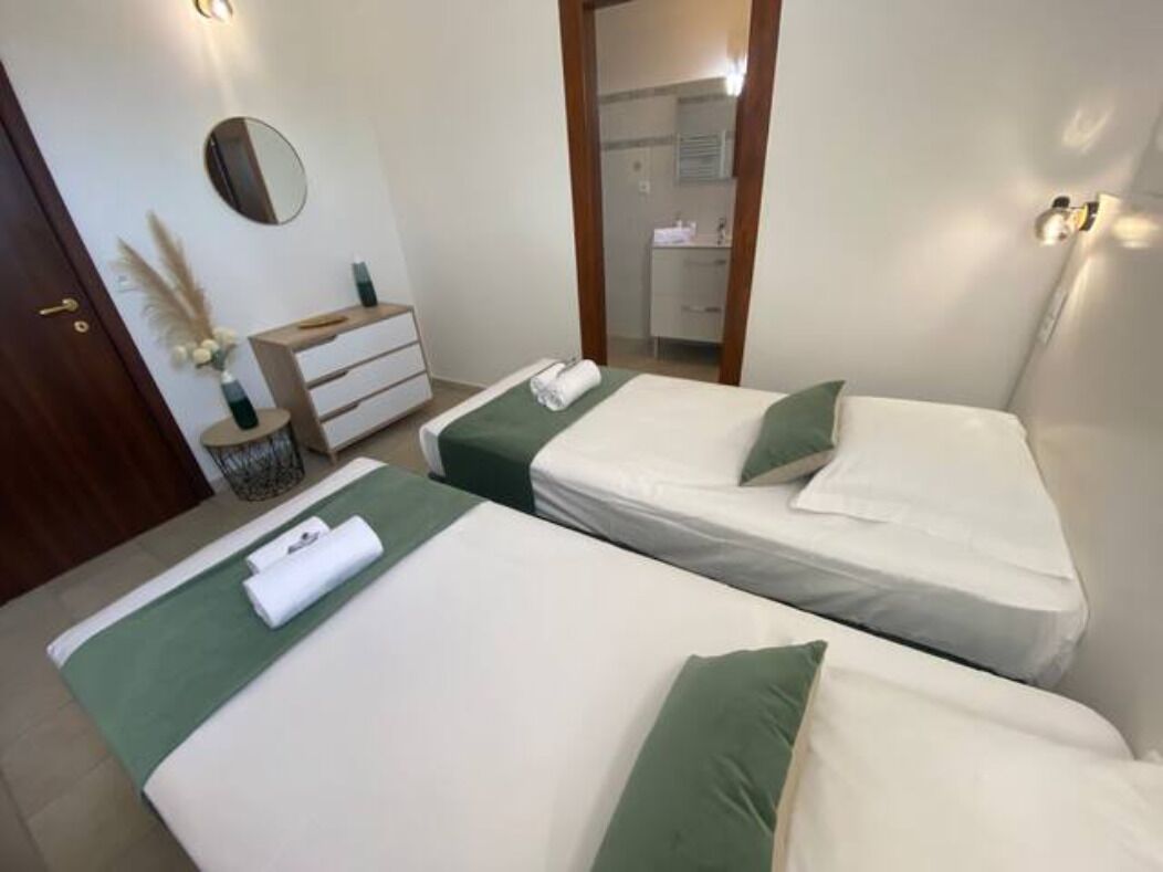 Une chambre d’hôtel avec deux lits, une commode, un miroir et une salle de bain visible à travers une porte ouverte.