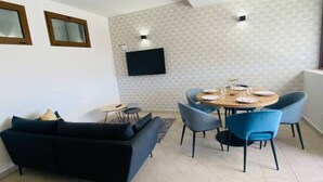 En moderne stue med en sort sofa, et spisebord med blå stole og et fladskærms-tv på væggen.
