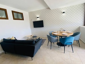 Un soggiorno moderno con un divano nero, un tavolo da pranzo con sedie blu e un televisore a schermo piatto montato a parete.