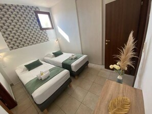 Camera d'albergo con due letti, un comodino in legno, un pannello decorativo a parete e una porta con finestra.