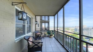 Un balcon avec deux fauteuils en osier et un pot de fleurs, donnant sur un paysage urbain.