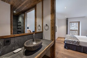 Une salle de bain moderne avec un lavabo en pierre, des poutres en bois et un grand miroir.