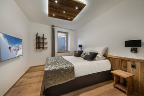 Une chambre à coucher avec un lit, une fenêtre, un plafond en bois, un téléviseur fixé au mur et un banc en bois.