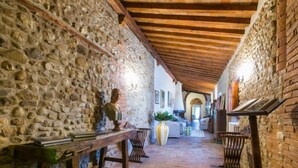A stone-walled corridor with a wooden bench, a table with books, and a vase with plants. - Il Convento by Interhome (Montefiridolfi)