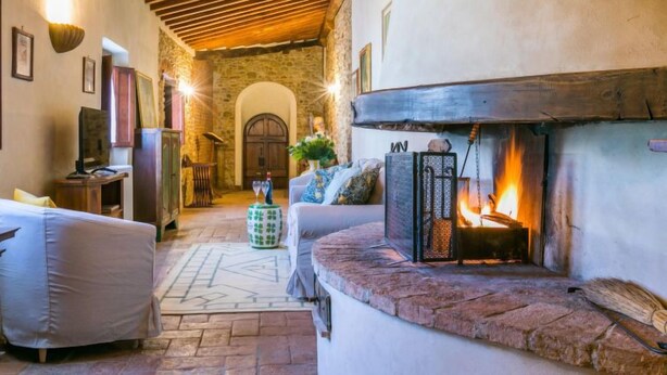 A cozy living room with a stone fireplace, wooden ceiling beams, and a stone wall. - Il Convento by Interhome (Montefiridolfi)