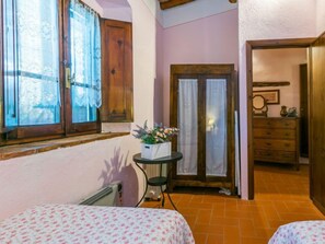 Ein gemütliches Zimmer mit einem Bett, einem kleinen Tisch mit einer Blumenvase, einer Heizung und einer Holztür, die in einen anderen Raum führt.