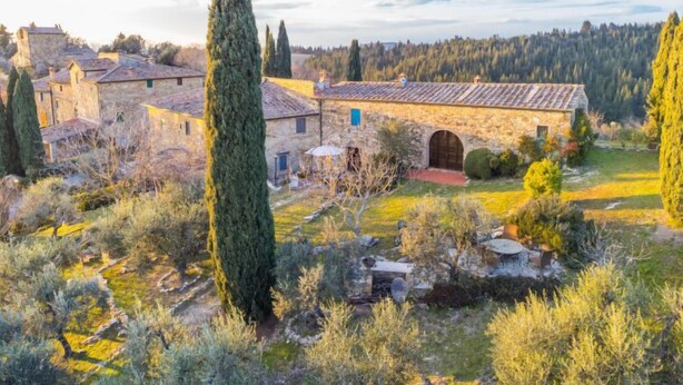 Un bâtiment rustique en pierre, doté d’un toit en tuiles, entouré d’oliviers et surplombant un ciel dégagé.