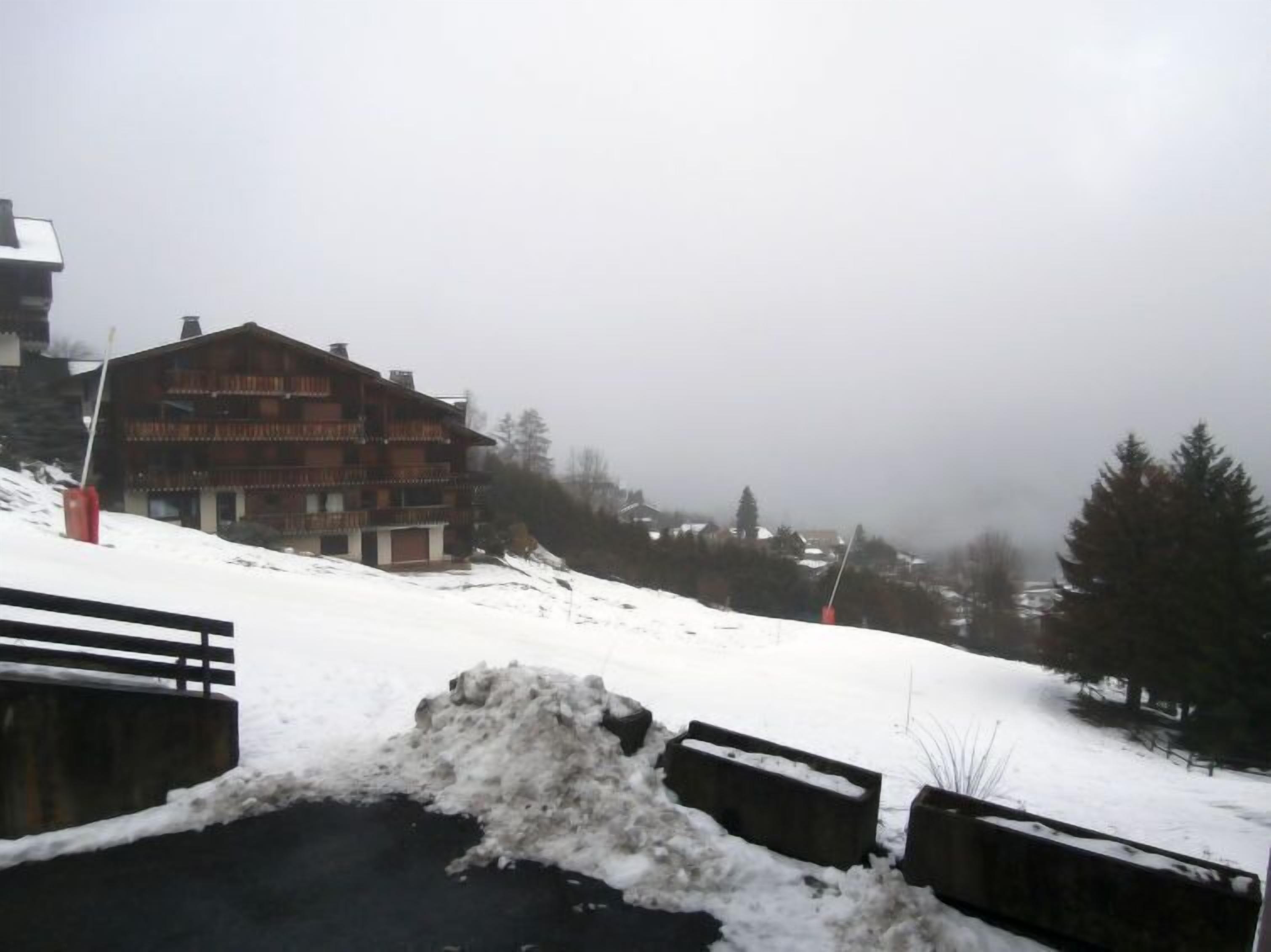 Paisaje nevado con un edificio de madera que tiene balcones, una valla de madera y un camino cubierto de nieve.