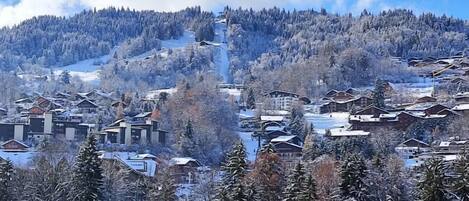 Un pueblo nevado en la montaña con casas de madera tradicionales, una pista de esquí y un cielo despejado.