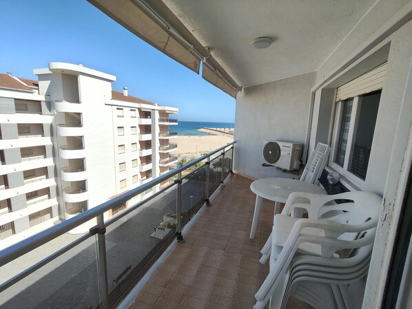 A balcony with a view of the beach, a table with chairs, and a Panasonic air conditioner.