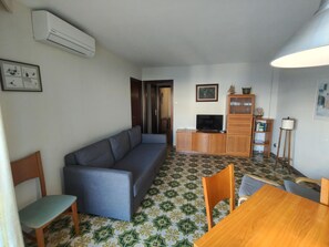 Een woonkamer met een bank, televisie, houten kast en een eettafel met stoelen.