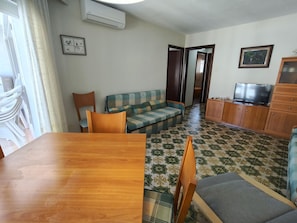 A room with a wooden dining table, a sofa, a television, and a cabinet. - Beachfront Apartment with Balcony, A/C, WiFi, and Underground Parking in Torredembarra (Torredembarra)