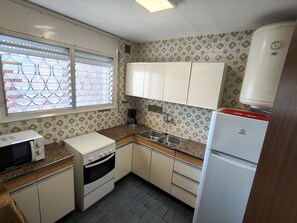 A compact kitchen with a microwave, oven, sink, and a refrigerator.