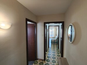 Un pasillo con puerta de madera, una lámpara, piso estampado y un espejo en la pared.