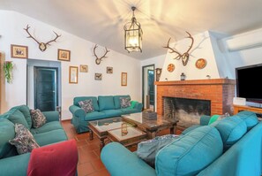 Ein Wohnzimmer mit Türkis-Sofas, einem Kamin, Geweihen an der Wand und einem Fernseher.