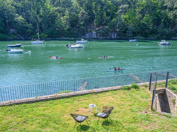 A lakeside view with boats, kayaks, and a grassy area with chairs and tables. - Glann Aven by Interhome (Le Bono)