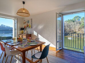A dining area with a wooden table set for four, a hanging light fixture, and a view of a natural landscape through large glass doors. - Glann Aven by Interhome (Le Bono)