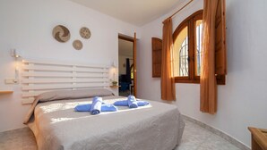 Un dormitorio con cama, mesita de noche, lámpara de pared y ventana con cortinas.