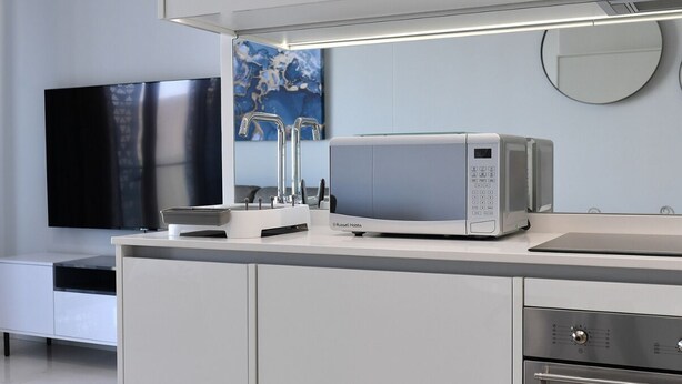 Een moderne keuken met een ingebouwde magnetron, een flatscreen televisie en een koffieapparaat.