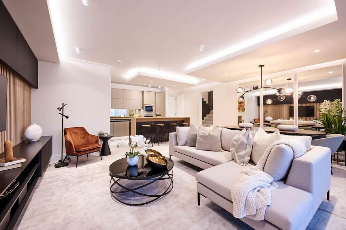 Ein modernes Wohnzimmer mit einer Couch, einem Couchtisch und einem Fernseher. Im Hintergrund ist eine Küche zu sehen.