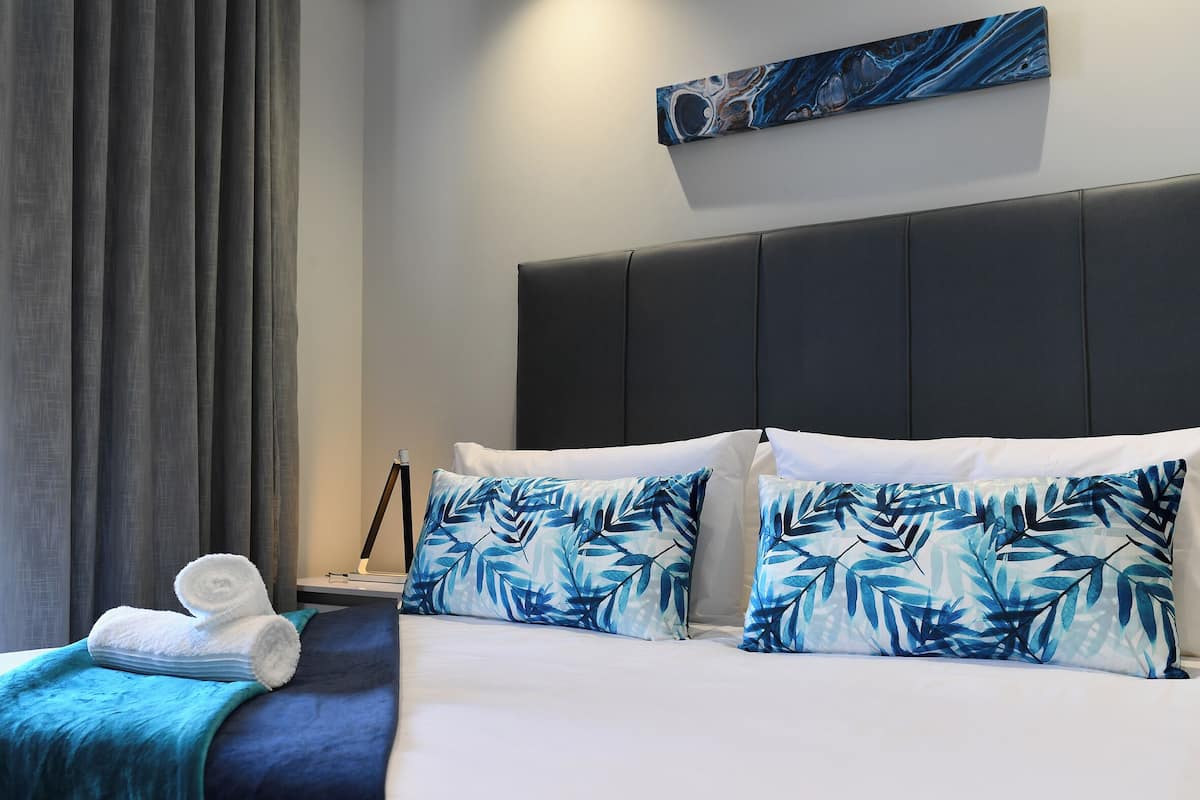 Ein Hotelzimmer mit Bett, Kissen, Decke, einem Gemälde und einem Nachttisch.