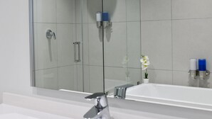 Een moderne badkamer met een douchecabine van glas, een witte wastafel en een kleine potorkidee.