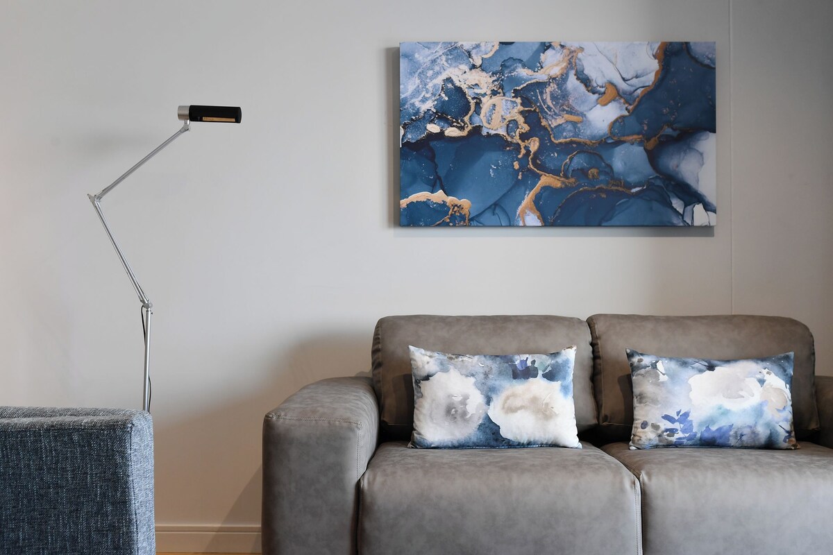 A modern living room with a gray sofa, two decorative pillows, a floor lamp, and a large abstract painting on the wall.