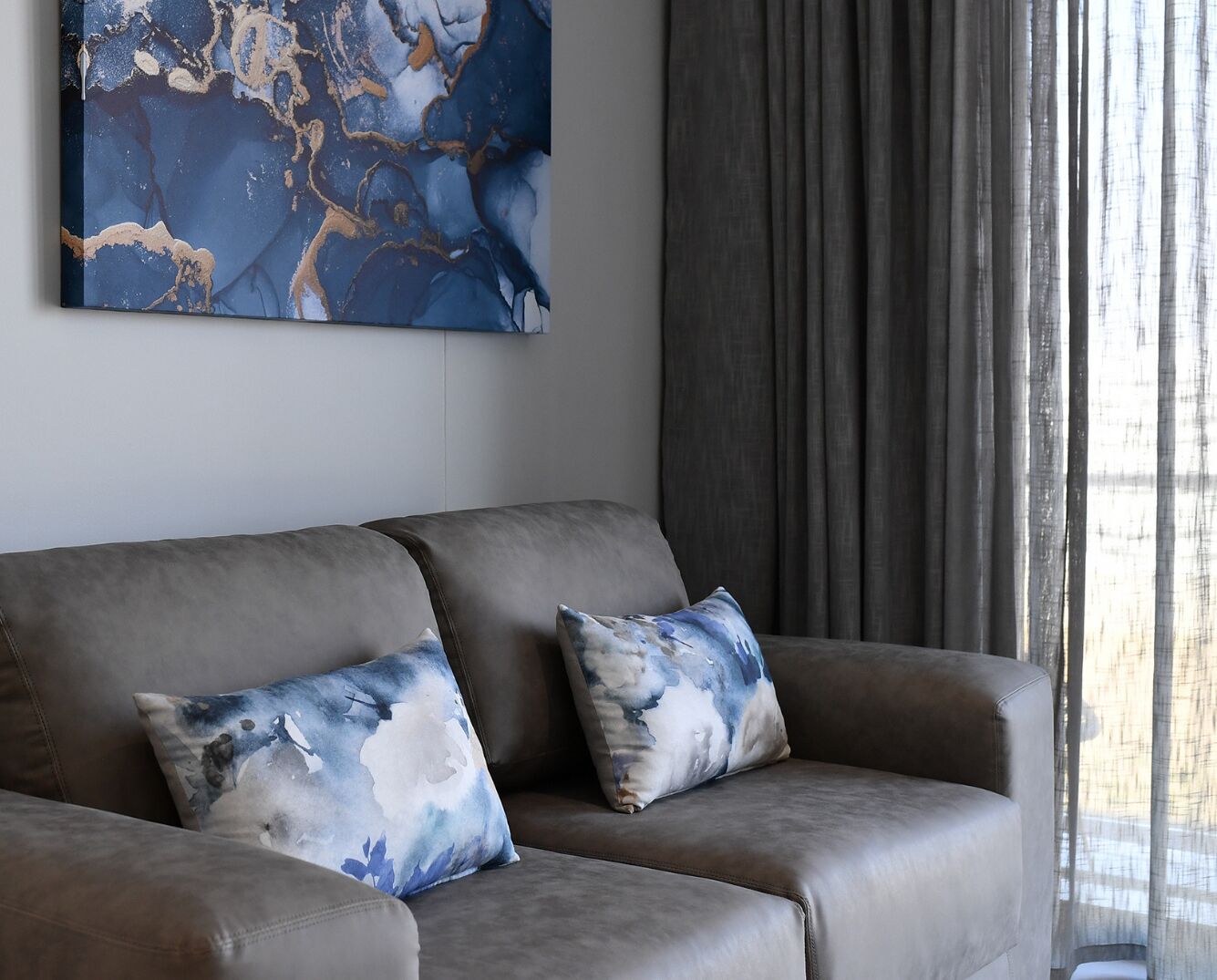 A modern living room with a grey sofa, two matching cushions, and a large abstract painting on the wall.