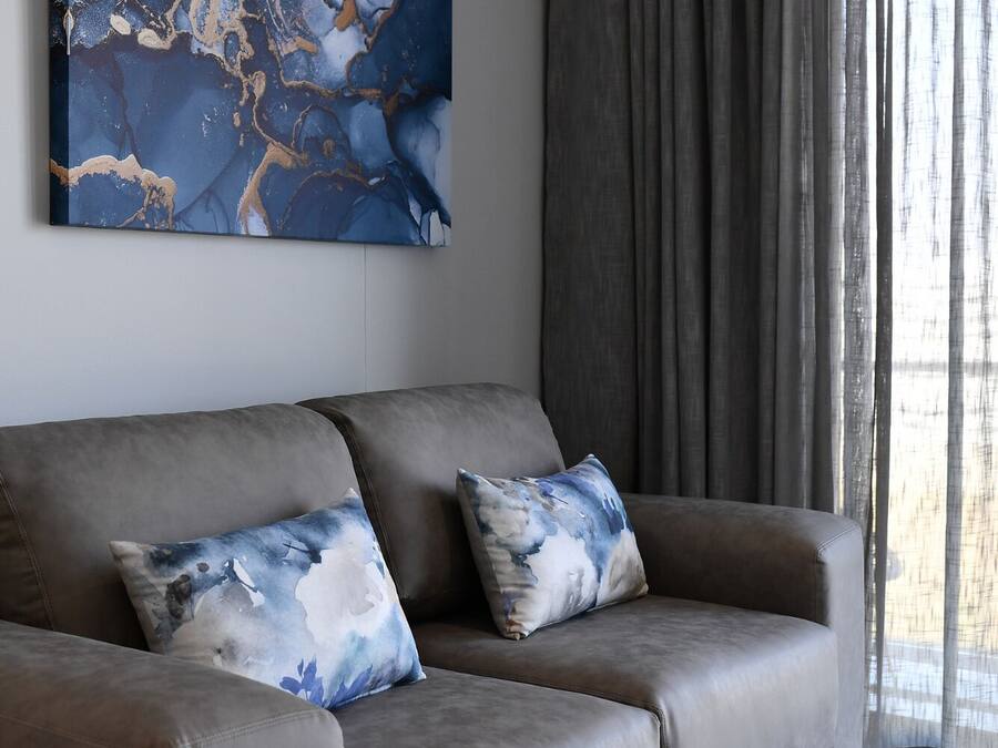 A modern living room with a grey sofa, two matching cushions, and a large abstract painting on the wall.