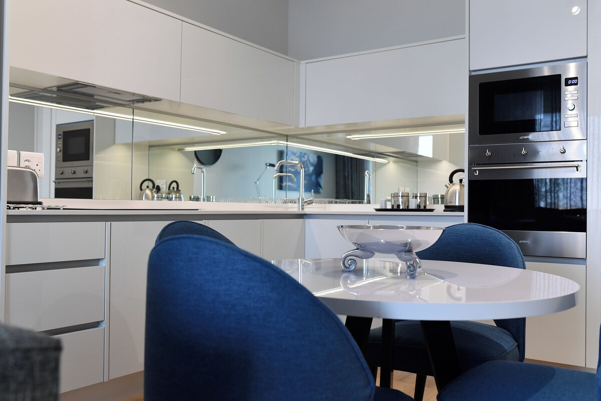 A modern kitchen with a central island, stainless steel appliances, and a dining area with blue chairs.