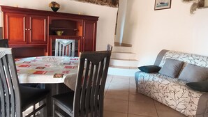 A dining area with a table, chairs, and a sofa. There is a staircase leading to an upper level. - An old oil press nestled between the sea and hiking trails (Santa-Reparata-Di-Balagna)