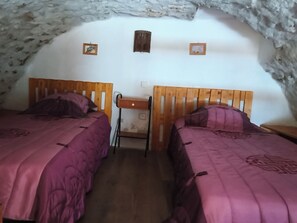 A cozy room with two wooden beds, a small table, and a stone wall.