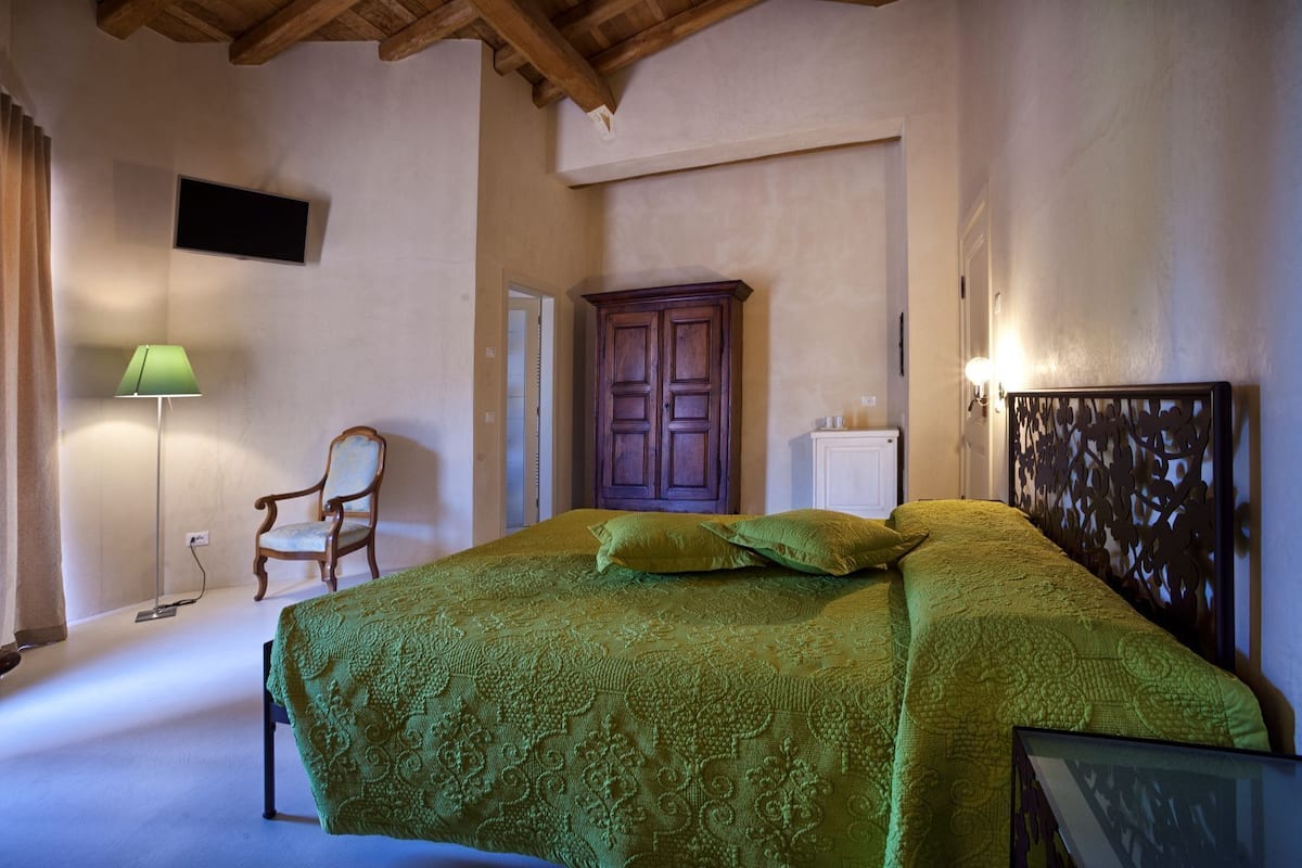 A bedroom with a large bed, a chair, a desk, a wardrobe, and a television.