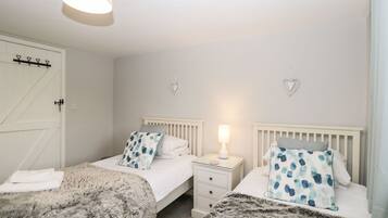 Een slaapkamer met twee bedden, elk voorzien van een wit hoofdeinde en een nachtkastje met een lamp. Er hangen hartvormige decoraties aan de muur en er is een witte deur met een klink.