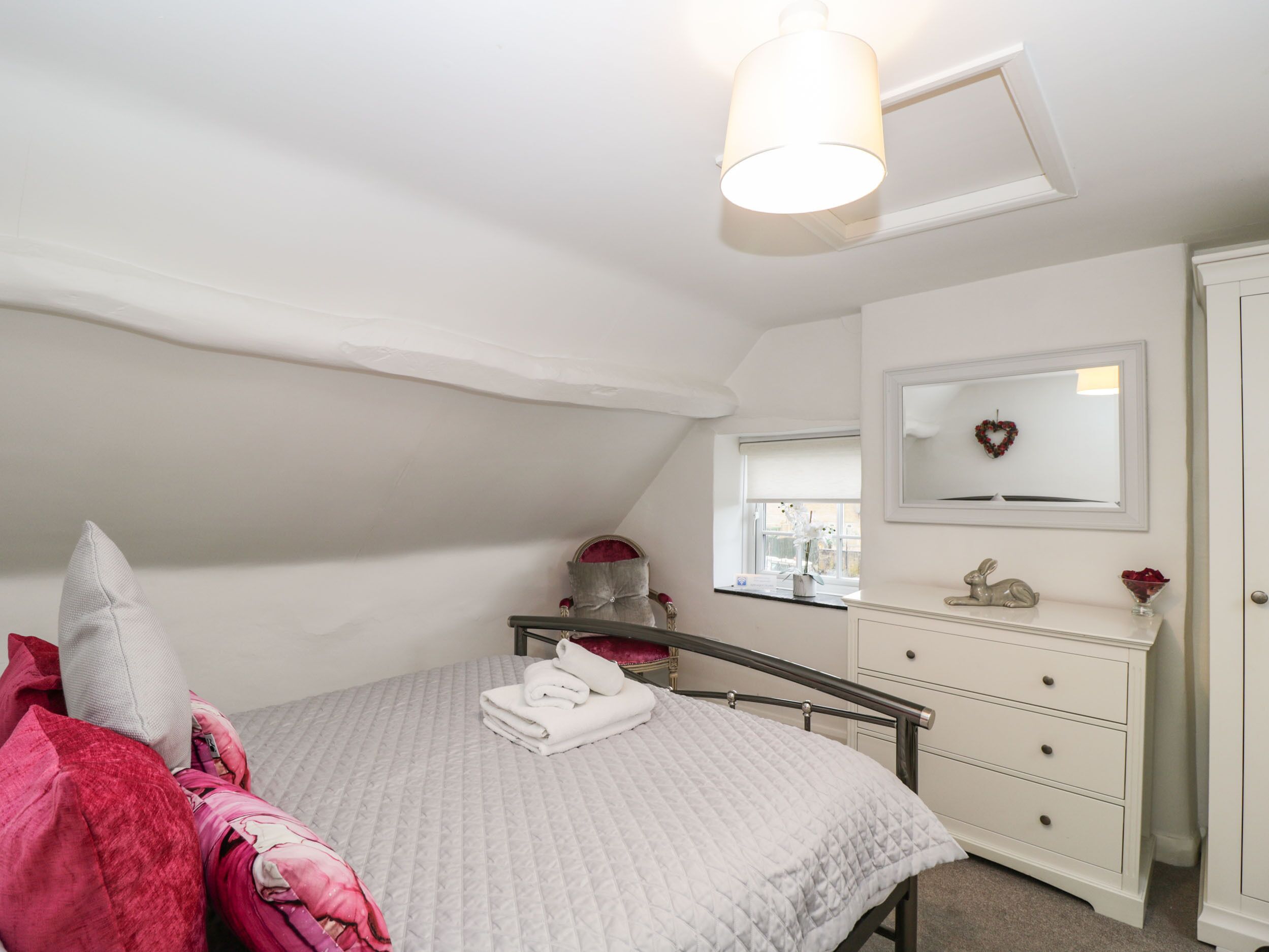 A bedroom with a bed, a dresser, a mirror, and a window.