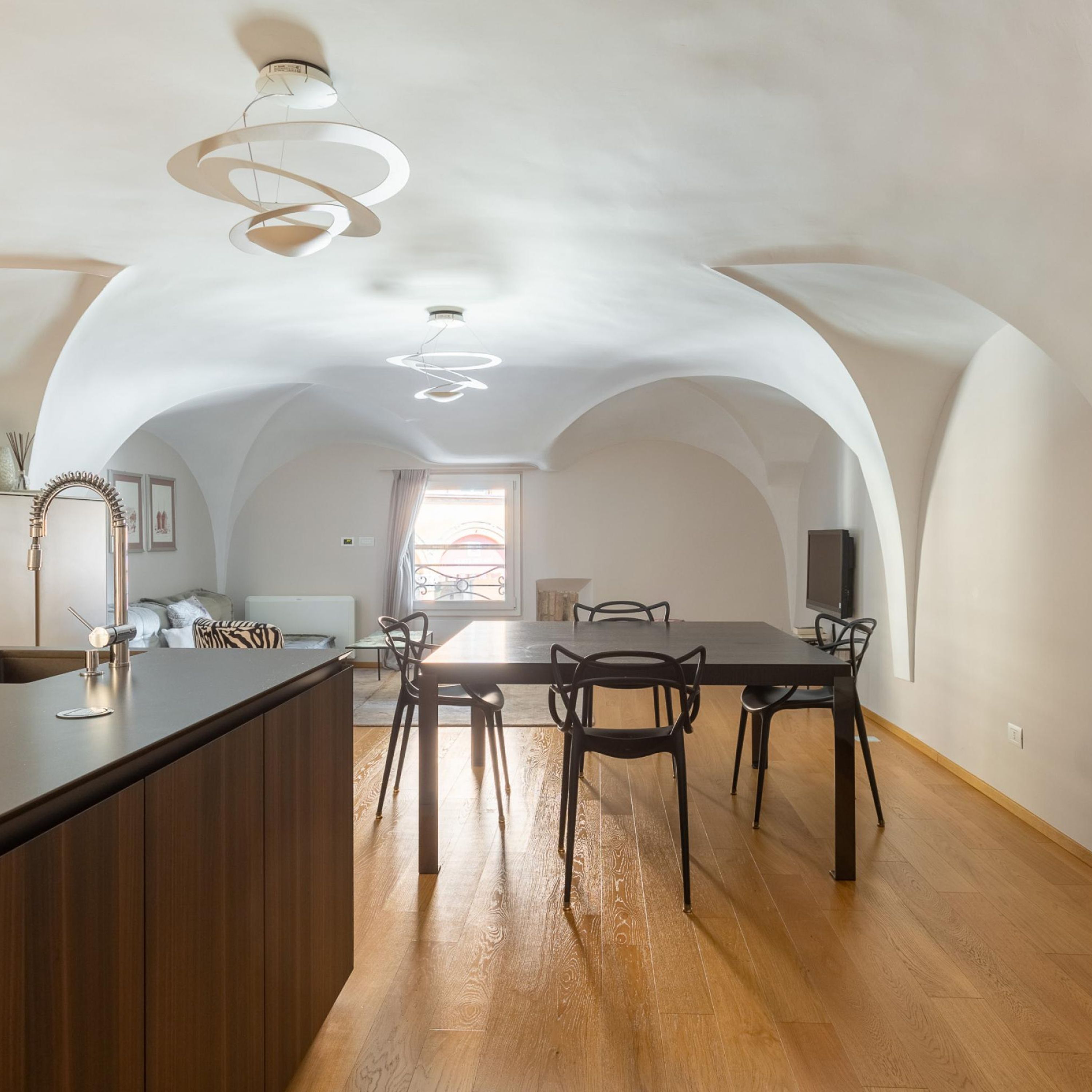 Un vaste espace de salle à manger avec une longue table et des chaises, un îlot de cuisine et un luminaire moderne au plafond.