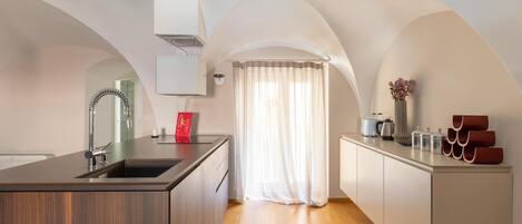Una cocina moderna con una isla central, un lavamanos empotrado y una ventana con cortinas traslúcidas.