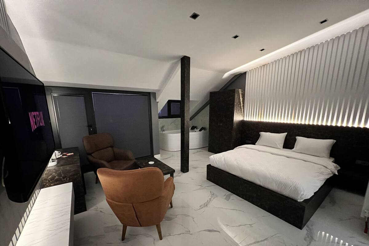 A modern hotel room with a large bed, a seating area with a chair, a TV, and a bathroom with a bathtub.