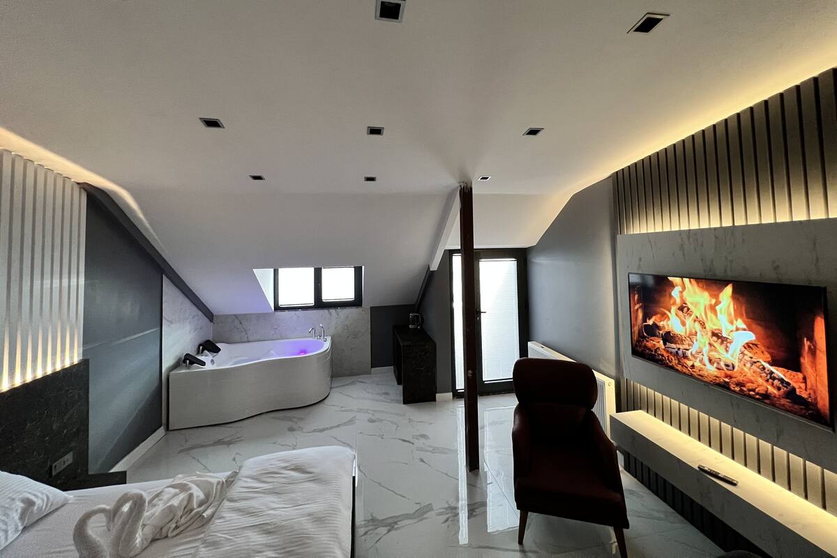 A modern hotel room with a large TV, a fireplace, a bathtub, and a cozy seating area.