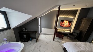 Un dormitorio moderno con una cama grande, un área de descanso con chimenea y un baño con bañera.