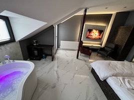 Un dormitorio moderno con una cama grande, un área de descanso con chimenea y un baño con bañera.